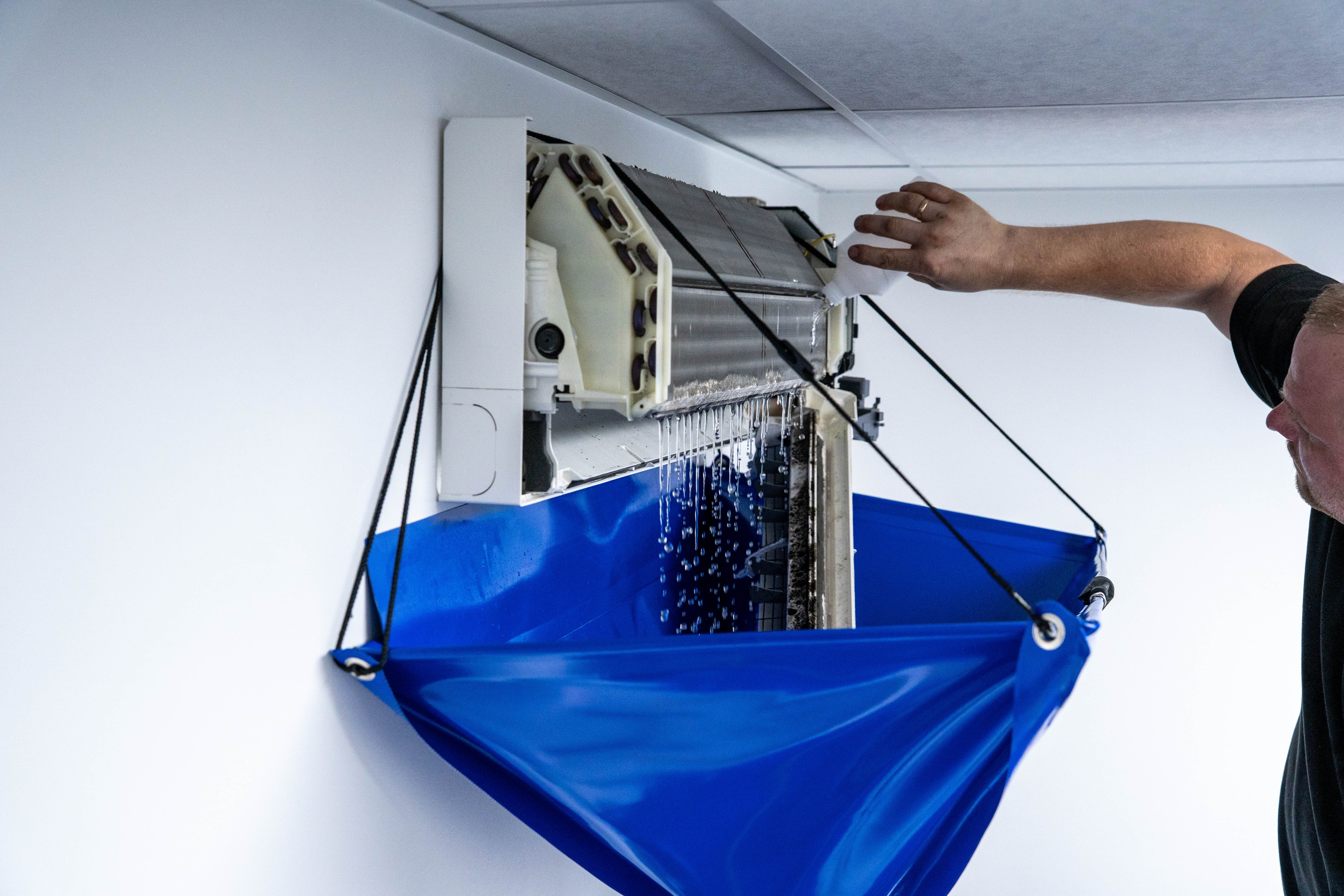 Handwerker macht eine Wartung an einer Klimaanlagen mit dem Falt-Trichter von DERLAUE®. Er lässt Wasser durch den Filter laufen.